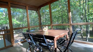 Une terrasse en bois avec une table et des chaises, de grandes fenêtres et un luminaire au plafond.