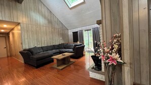 Un salon spacieux avec un grand canapé d’angle noir, une table basse en bois et un vase rempli de fleurs.