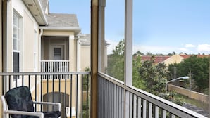 Un balcon avec une chaise, une vue sur les bâtiments voisins et un ciel dégagé.