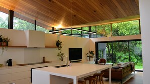 A modern kitchen with a central island, wooden ceiling, large windows, and a cozy seating area with a sofa and chairs. - Private Architectual Beach Retreat in Pearl Beach (pearl beach)