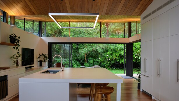 A modern kitchen with a central island, wooden ceiling, and large windows offering a view of greenery. - Private Architectual Beach Retreat in Pearl Beach (pearl beach)
