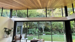A modern interior with a wooden ceiling, large windows, and a view of a lush garden. - Private Architectual Beach Retreat in Pearl Beach (pearl beach)
