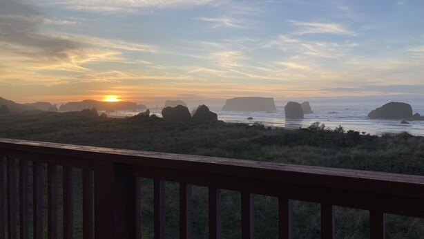 A coastal landscape with a wooden deck in the foreground, overlooking a beach with large rock formations and the ocean. - Dunes House at Bandon - 3 bedroom Oceanfront (Bandon)