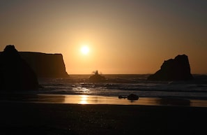 A beach scene with large rock formations and the sun setting over the ocean.