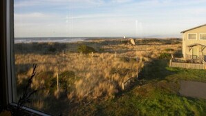 A coastal view from a window overlooking a grassy area with a small building and a fence. - Dunes House at Bandon - 3 bedroom Oceanfront (Bandon)