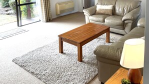 Een woonkamer met een beige bank, een houten salontafel en een bijzettafeltje met een lamp en een plant.