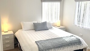 Een slaapkamer met een groot bed, twee nachtkastjes met lampen, een raam met gordijnen en een deur met gouden handvat.