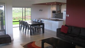 Una sala de estar moderna con comedor, cocina y un amplio ventanal corredera que da a un jardín.