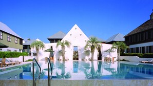 Et hotel med swimmingpool, palmer og en hvid bygning med et ur.