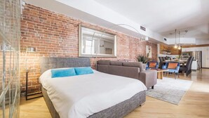 Ein modernes Schlafzimmer mit einem großen Bett, einem grauen Sofa und einem Essbereich mit Tisch und Stühlen.