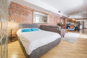 A modern bedroom with a large bed, a grey sofa, and a dining area with a table and chairs. - MTLVR #07| Unique flat near downtown, central AC (Montreal)