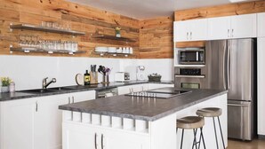 Een moderne keuken met een centraal eiland, houten wandbekleding, witte kasten en roestvrijstalen apparatuur, en barstoelen.