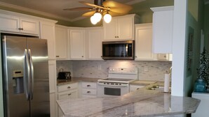 A kitchen with white cabinets, a stainless steel refrigerator, a microwave, a stove, and a sink. - Oceanfront Home- Casa Del Sol- Live the LIFE!  4 decks, beach gear, grill... (St Augustine Beach)