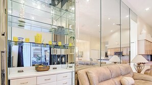 Ein modernes Wohnzimmer mit einem beigefarbenen Sofa, einer Vitrine mit Dekorationen und einem großen Spiegel, der den Raum reflektiert.