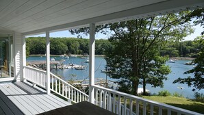 A wooden deck with a railing overlooking a lake with boats and docks. - Waterfront Cottage in South Bristol w/ private dock and lobster boat views (South Bristol)