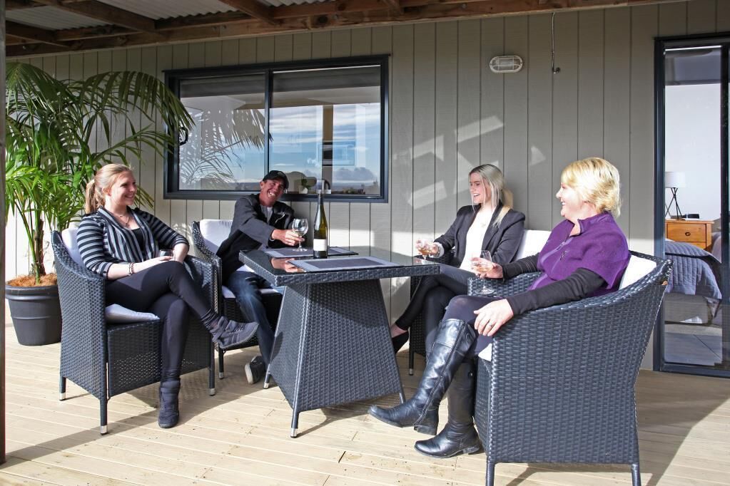 A group of four people seated around a table in an outdoor patio area with wicker furniture and a view of the ocean.
