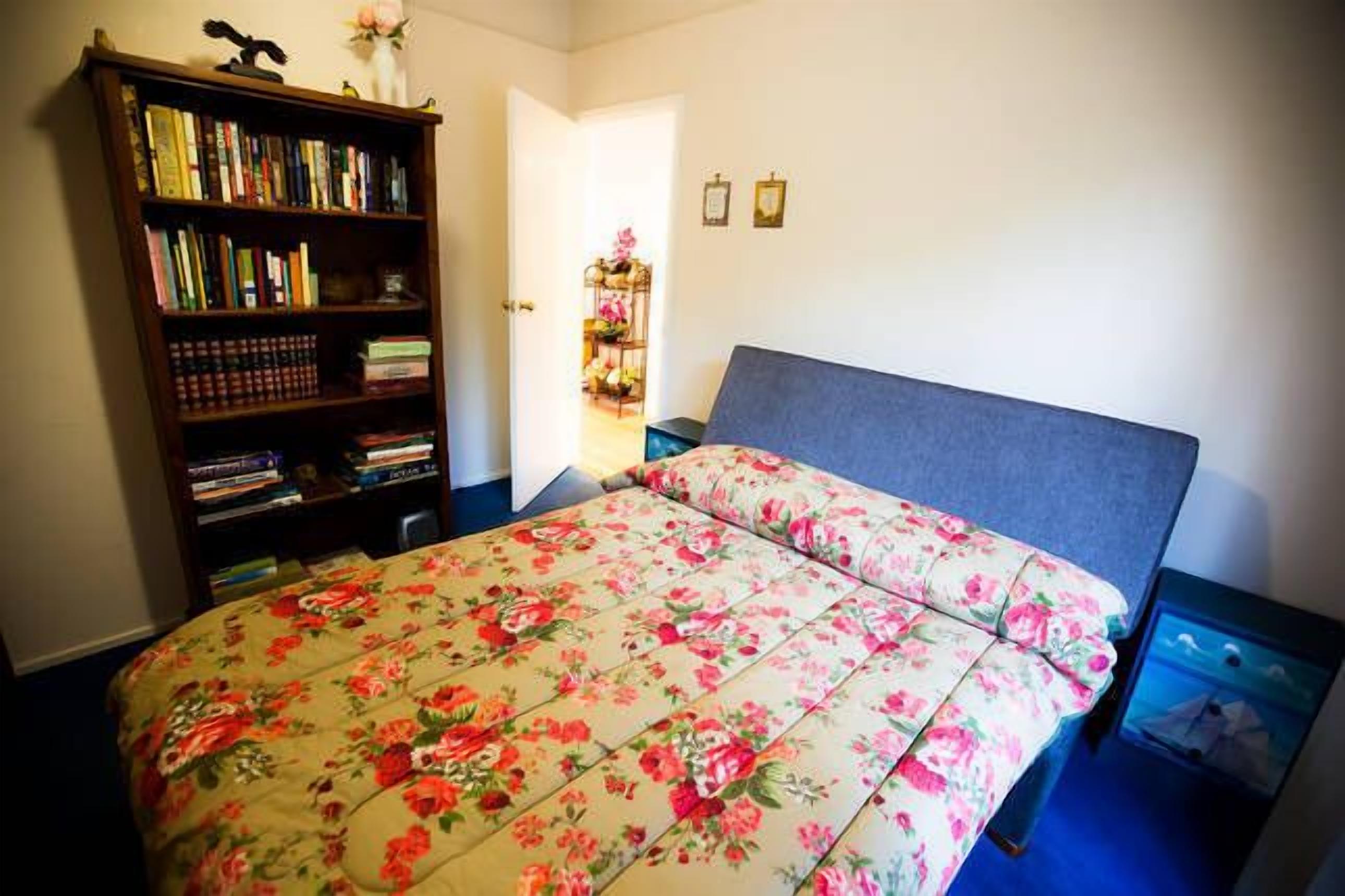 A bedroom with a bed, a bookshelf, and a nightstand.