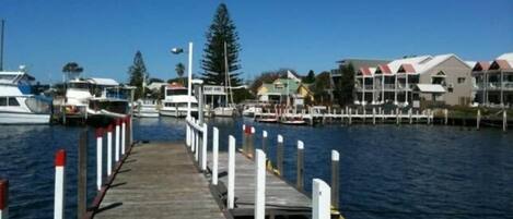 A wooden pier leading to a marina with boats docked, surrounded by buildings with red roofs.