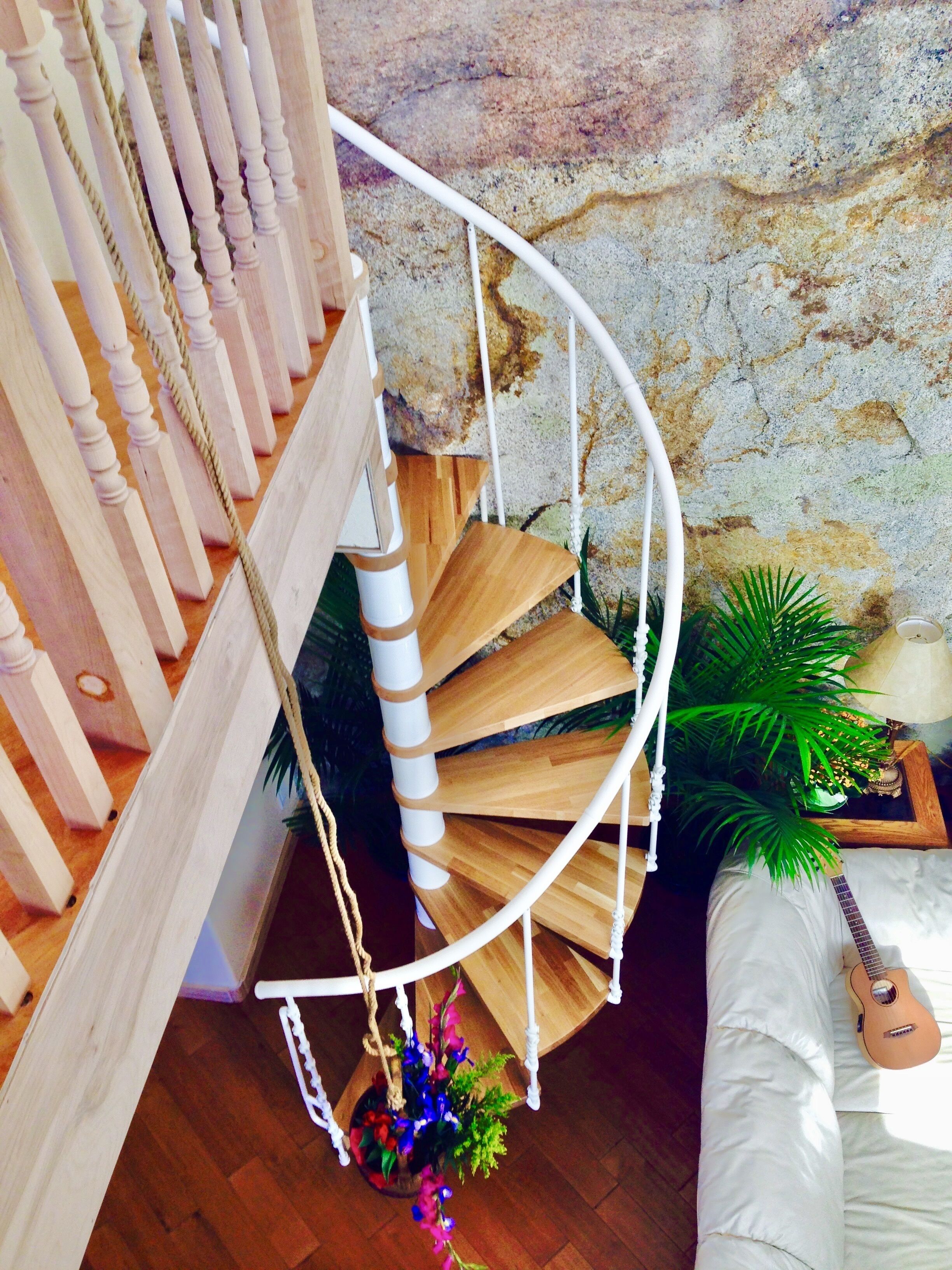 Un escalier en colimaçon avec des marches en bois et des rampes blanches, menant à une pièce où se trouvent une guitare et une plante.