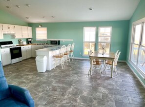 Una cocina amplia con armarios blancos, una isla central con taburetes y un comedor con mesa y sillas de madera.