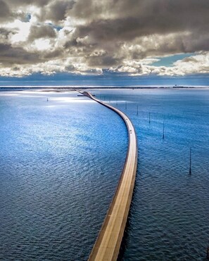 Een kustweg kronkelt door het water, met een bewolkte lucht erboven.