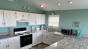 Una cocina moderna con gabinetes blancos, encimera de granito, horno empotrado, microondas y cafetera.