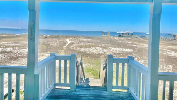Una terraza de madera con barandas blancas que da a vista de la playa.
