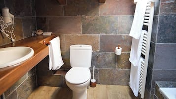 Un baño con tocador de madera, lavamanos blanco, inodoro y zona de ducha.