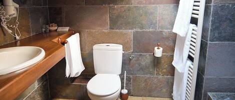 A bathroom with a wooden vanity, white sink, toilet, and a shower area.
