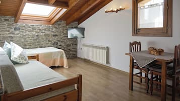 Um quarto aconchegante com parede de pedra, vigas de madeira no teto, uma cama, uma mesa com cadeiras e uma TV fixada na parede.