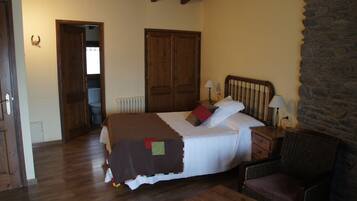 Ein Schlafzimmer mit Bett, Sessel, Nachttisch, Lampe und Steinwand.