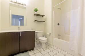 A bathroom with a toilet, sink, mirror, shelves, and a bathtub. - Sage Apartments Atlanta at Old 4th Ward (Atlanta)