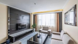 Una sala de estar moderna con un televisor de pantalla plana, una mesa de centro, sofás y un ventanal con cortinas.