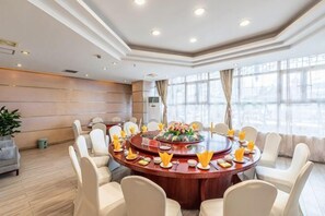 Un salón de conferencias con una mesa redonda, sillas blancas y un ventanal grande.