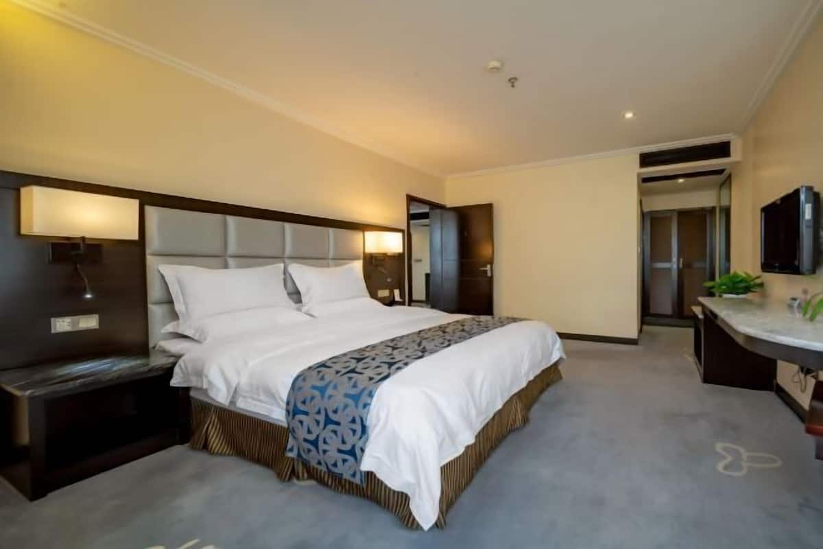 A modern hotel room with a large bed, bedside tables, a desk, and a flat-screen TV.