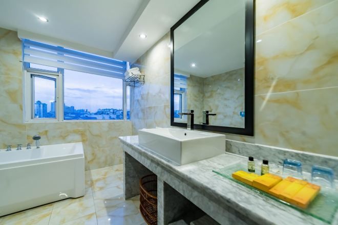 A modern bathroom with a large window, a bathtub, a vanity with a mirror, and a marble floor.