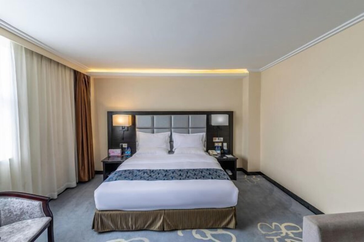 Quarto de hotel com uma cama grande, uma mesinha de cabeceira, uma luminária e uma cadeira.