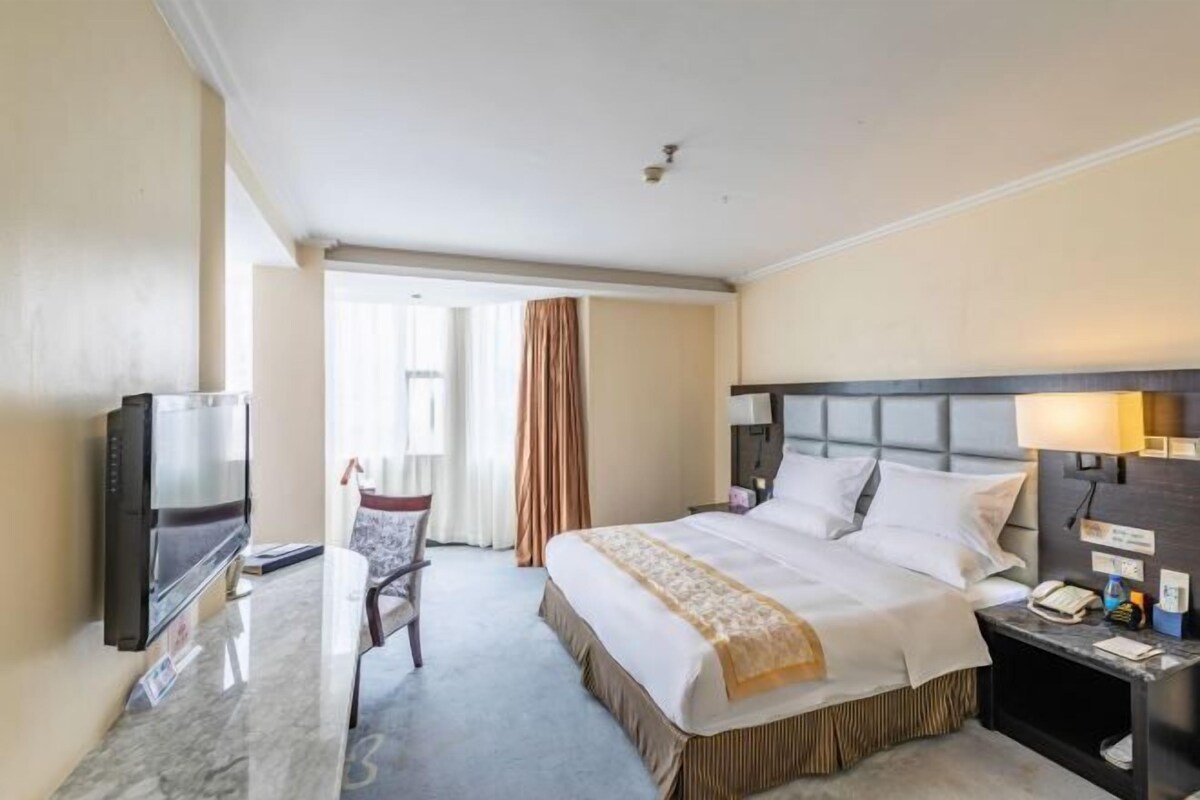Quarto de hotel com cama, televisão, escrivaninha e cadeira.