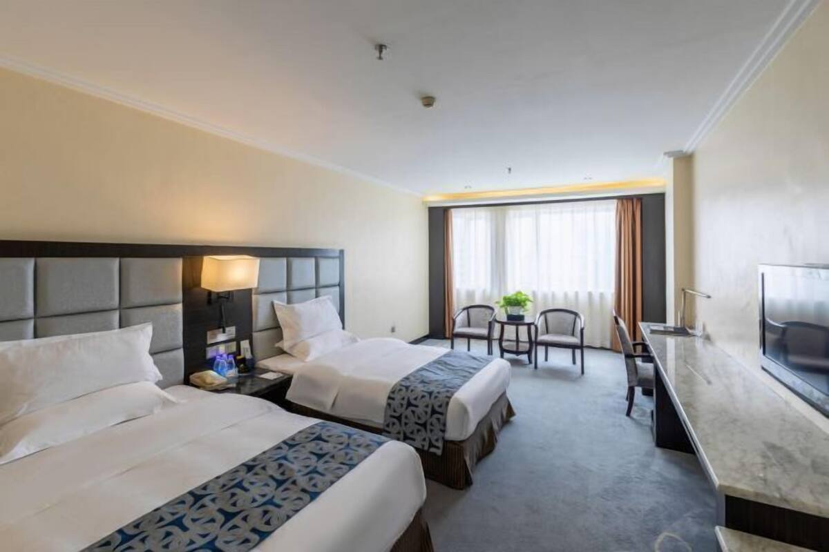 A hotel room with two beds, a desk, a chair, and a TV.
