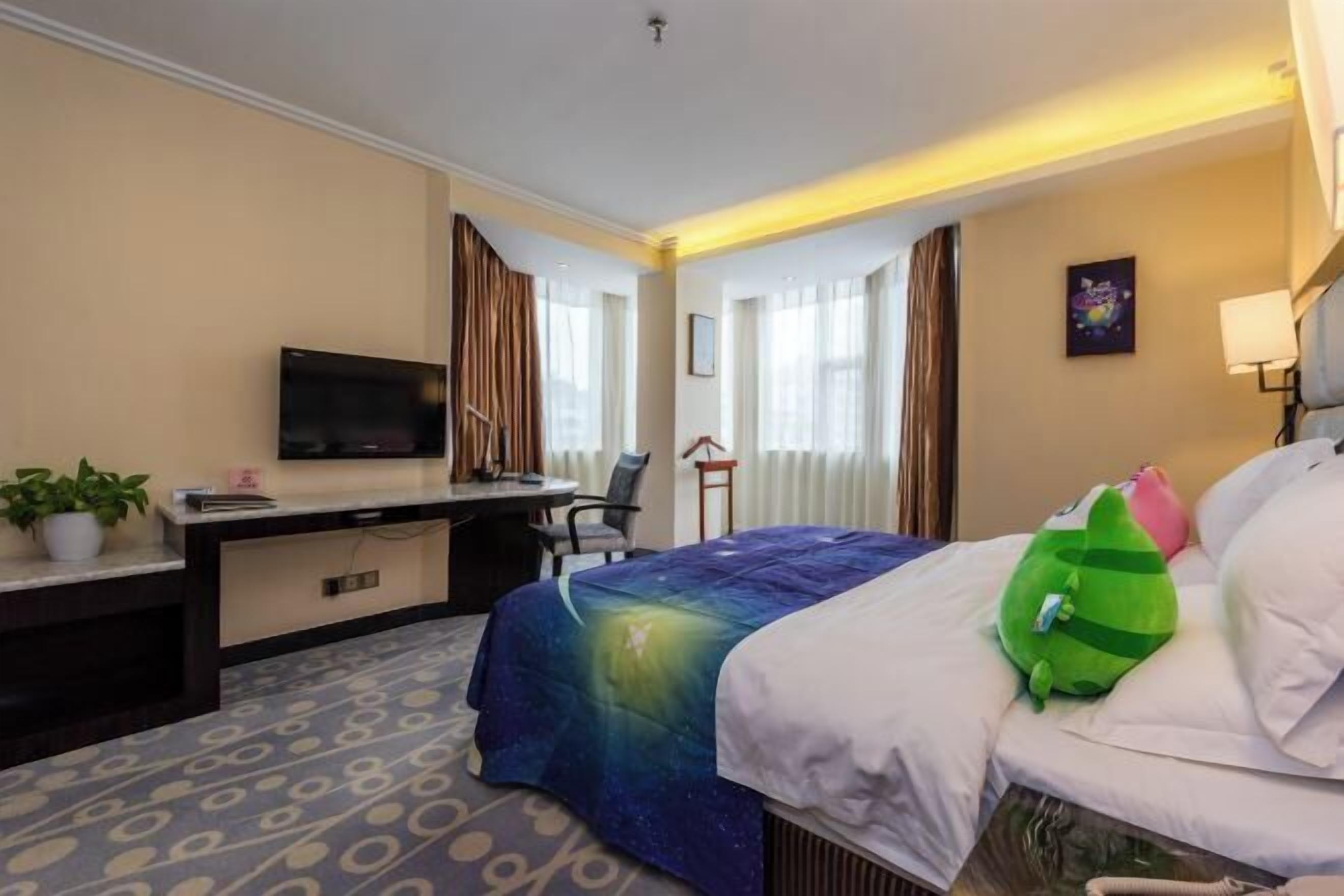 Ein Hotelzimmer mit Bett, Schreibtisch, Fernseher, Stuhl und einem fenster mit Vorhängen.