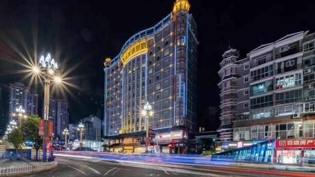 Un hotel de varios pisos con una estructura destacada en esquina, señalización iluminada y una calle bien iluminada al frente.