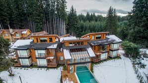 Un complejo moderno de cabañas de madera con varias construcciones interconectadas, una piscina central y un bosque nevado de fondo.