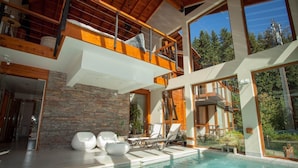 Una casa moderna con un amplio balcón de vidrio, piscina y un muro de piedra.