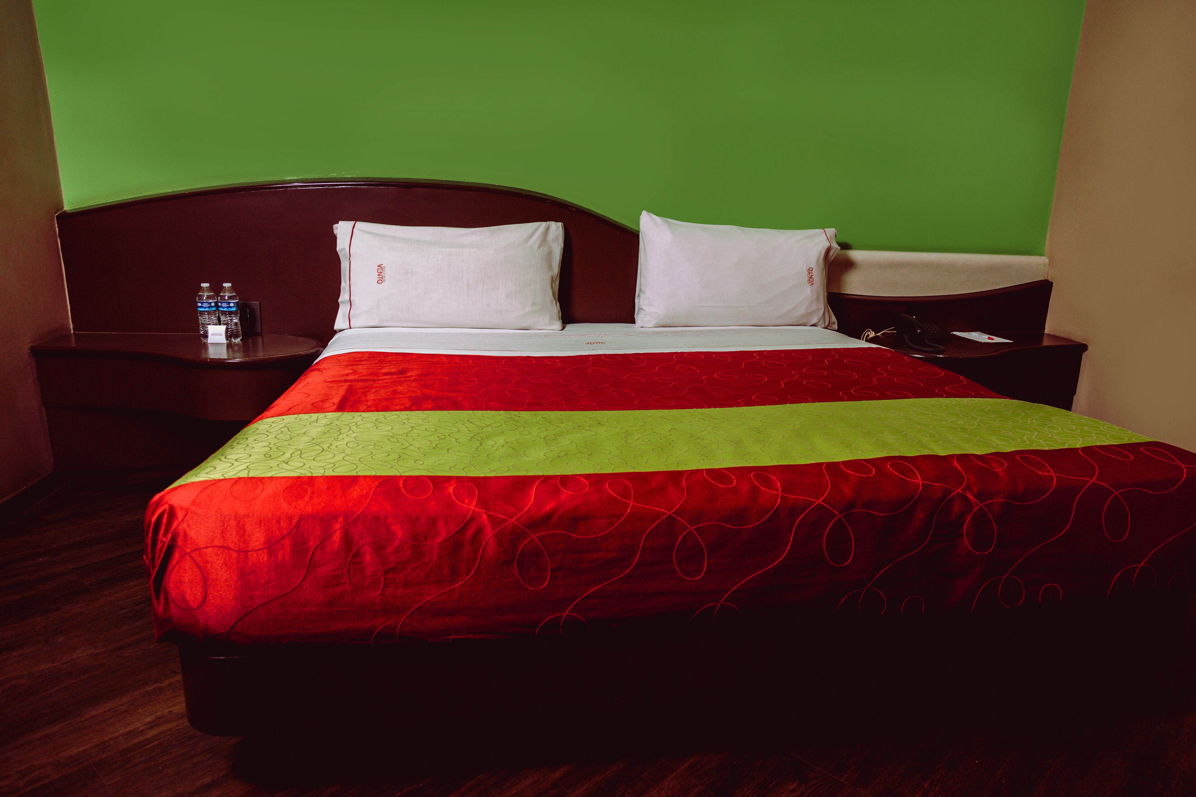 Una habitación de hotel con una cama, paredes verdes y un cabecero de madera.