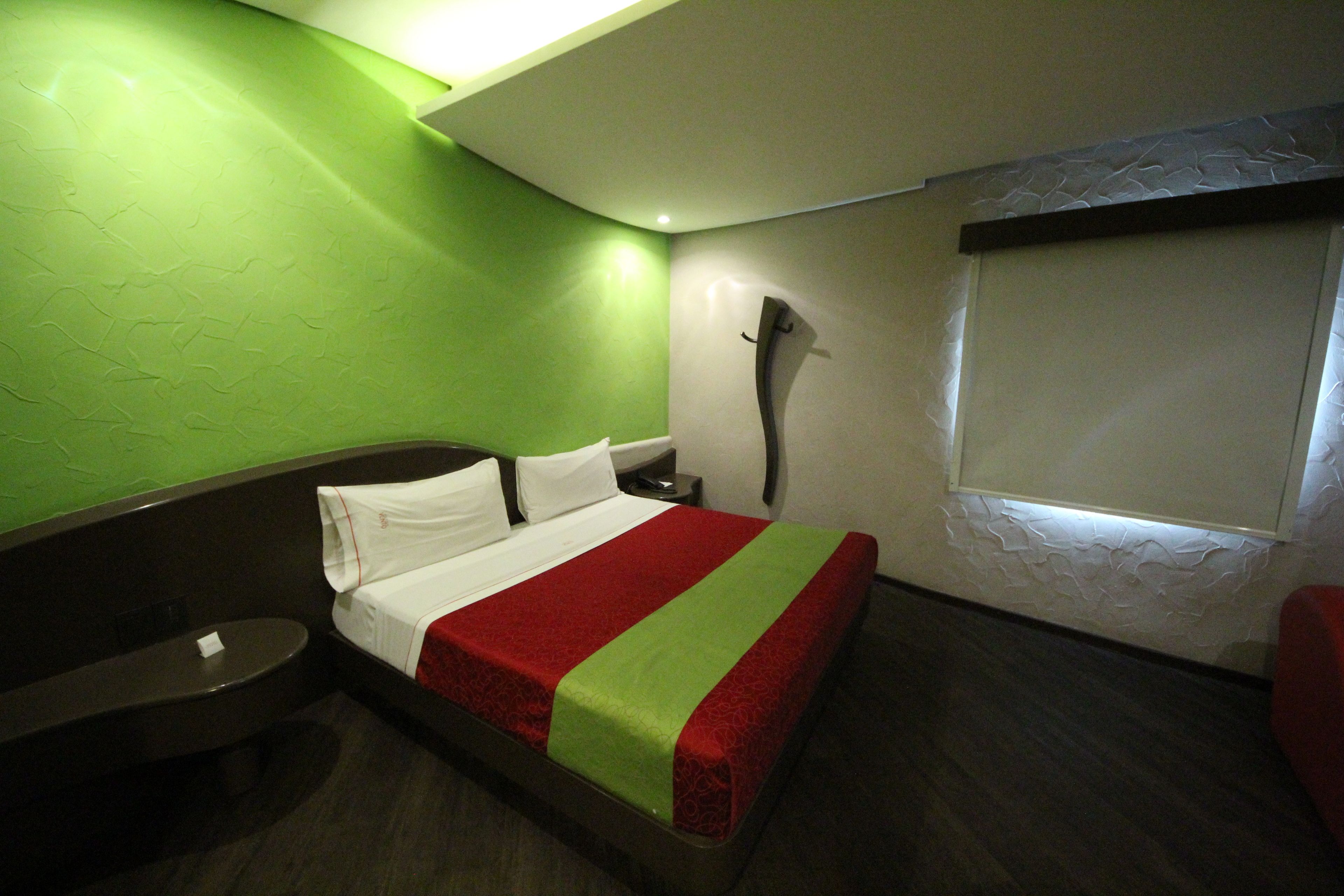 Una habitación de hotel con una cama, una mesita de noche, un espejo y una ventana con persianas.