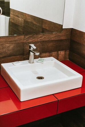 Un lavabo blanc, installé dans une salle de bain, doté d’un robinet moderne, se démarque sur un plan de toilette rouge et un mur revêtu de panneaux en bois.