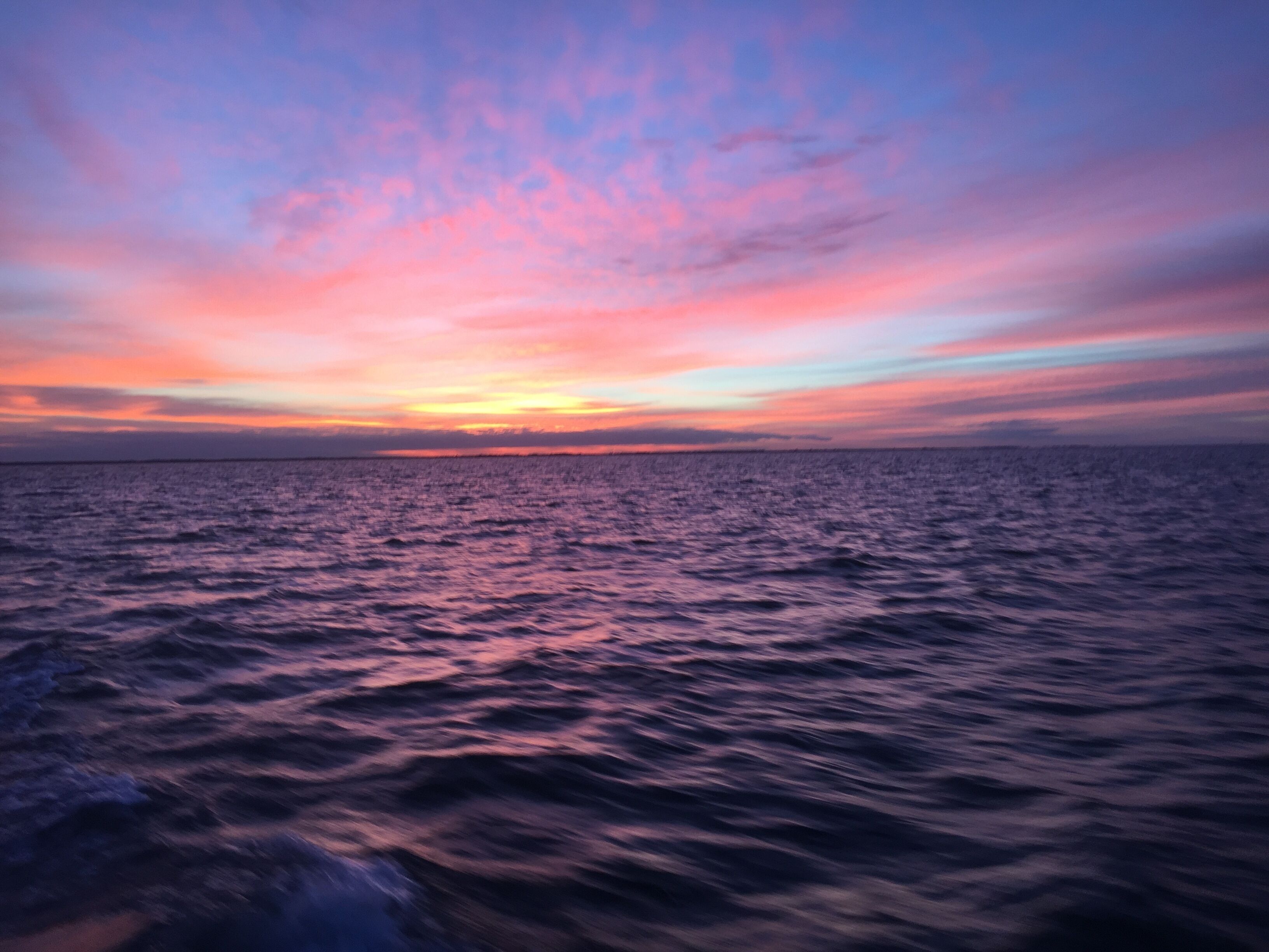 Een zonsondergang boven een rustige zee met een heldere horizon.