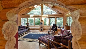A log cabin interior with a high ceiling, wooden furniture, and large windows offering a view of the forest. - Secluded luxury log home in Wisconsin wilderness (Clam Lake)