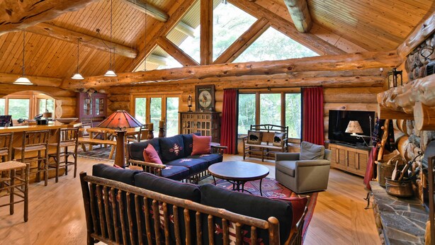 A spacious log cabin interior with a large dining area, a cozy living room with a fireplace, and a television. - Secluded luxury log home in Wisconsin wilderness (Clam Lake)
