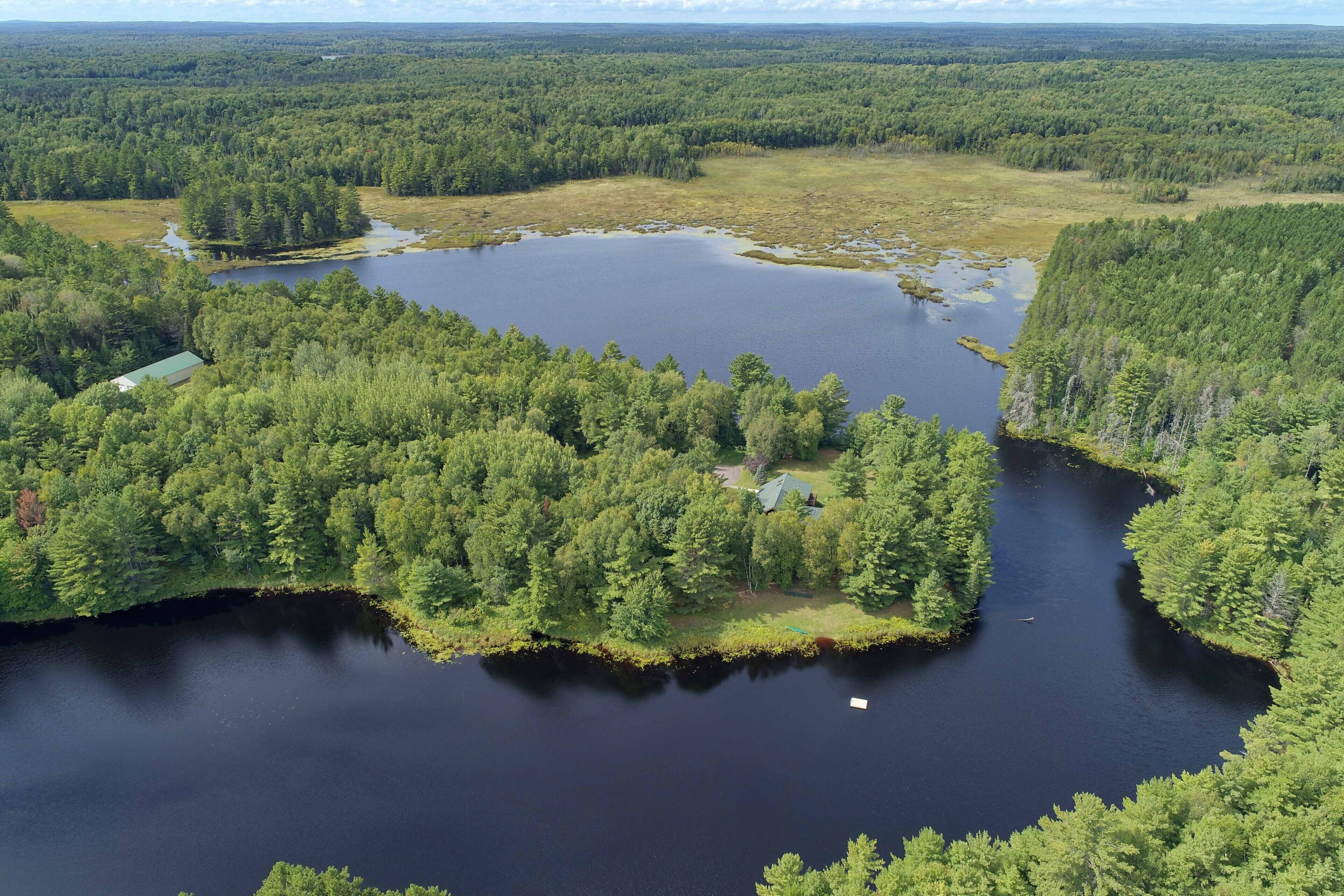 Une vue aérienne d’une zone boisée avec un lac, entourée d’arbres denses et d’un petit bâtiment.